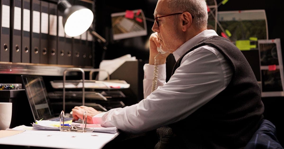 Photograph: Tired senior investigator thinking at solution to catch supect, working late at night at criminal case in dark.