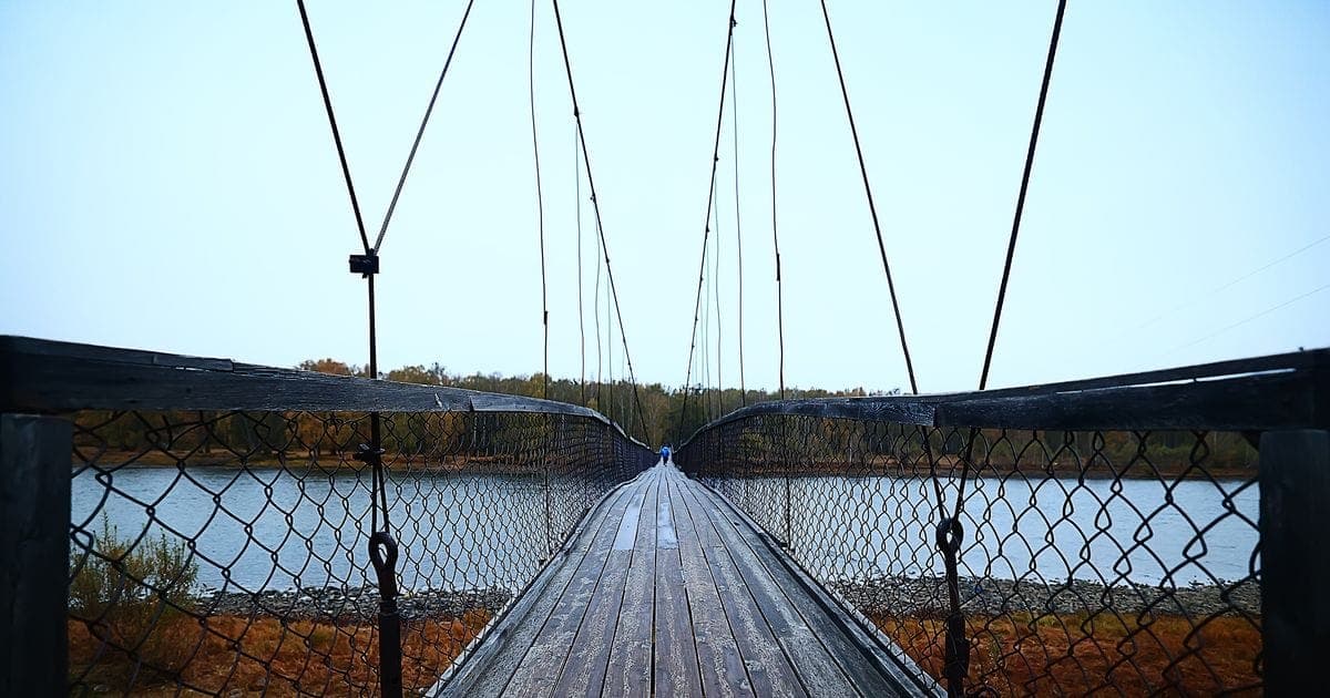Photograph: suspension bridge across the river, altai view dilapidated old bridge crossing.